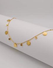 Dainty gold necklace with hammered coins and zircon drops on white background
