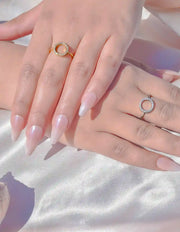 Two hands wearing gold and silver rings on a light background