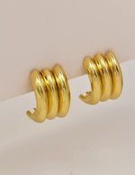 Triple gold conch earrings displayed on soft beige card